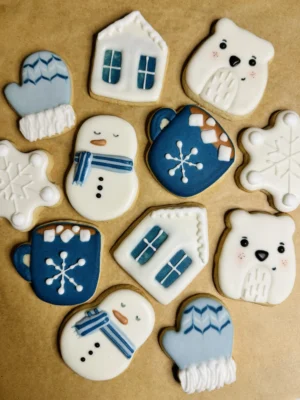 Mini winter themed cookies with snow covered house, polar bear, snowman, mitten, snowflakes, and mug of hot chocolate with marshmallows